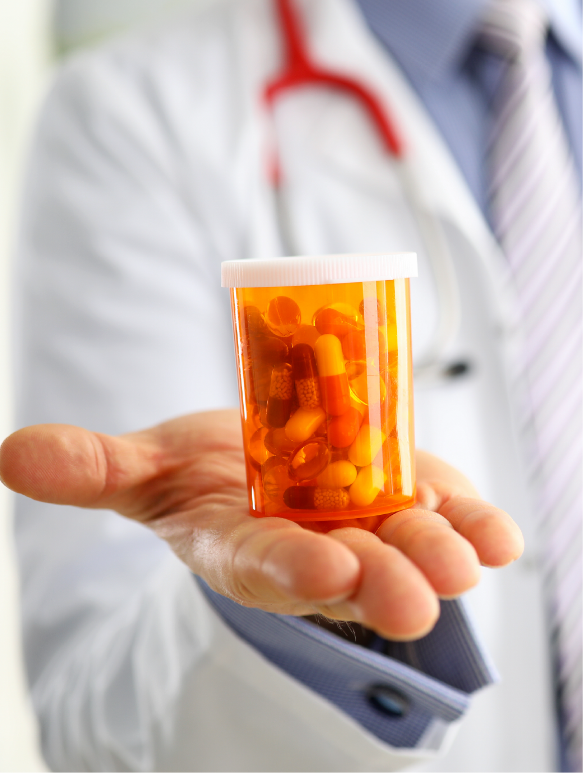 Doctor in white coat holding a prescription medication bottle filled with capsules and pills