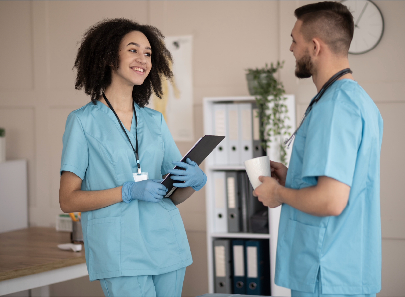 Two medical professionals in teal scrubs discussing patient care in a clinical office setting