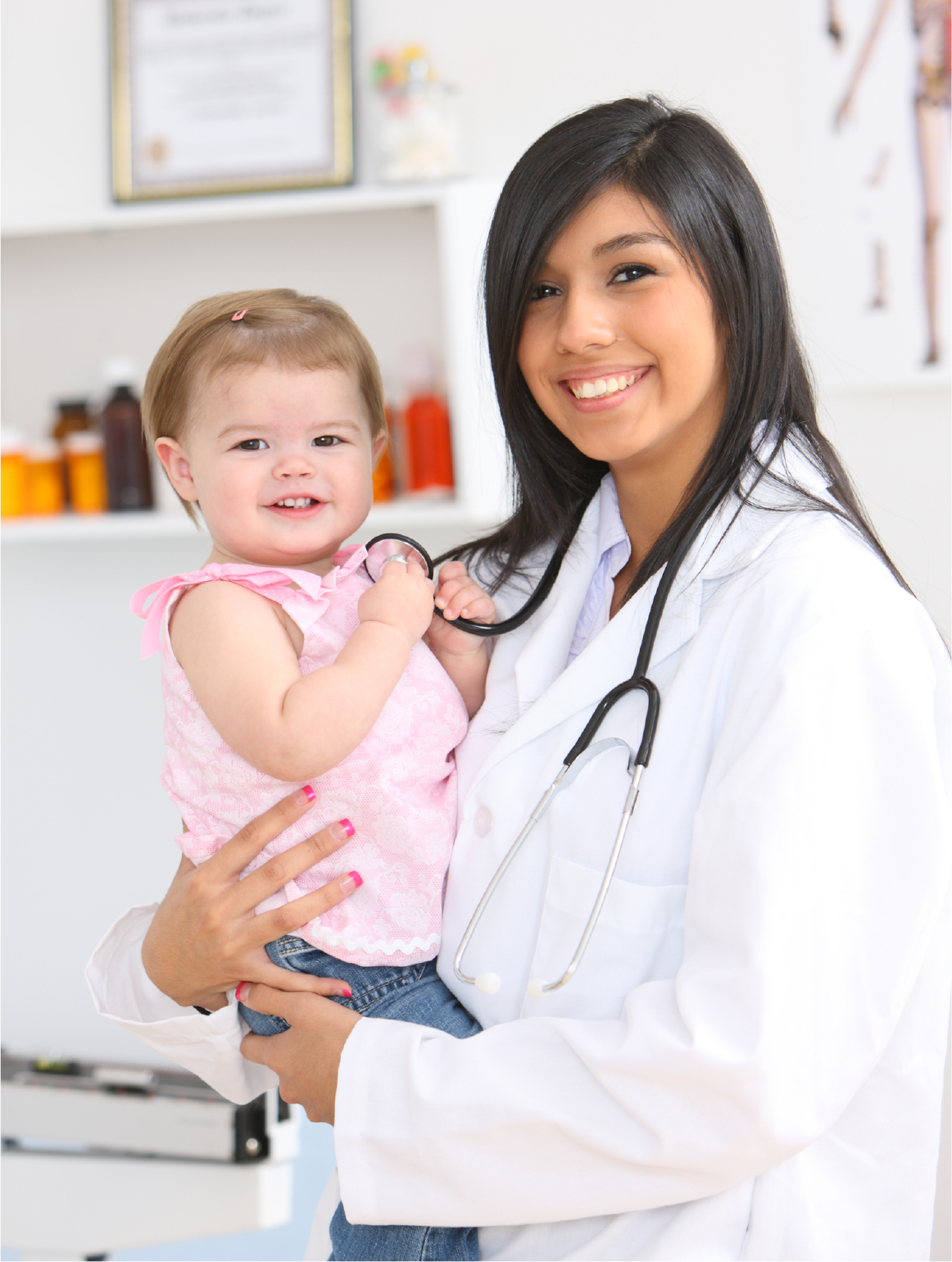 Smiling female pediatrician in white lab coat holding happy baby girl with stethoscope